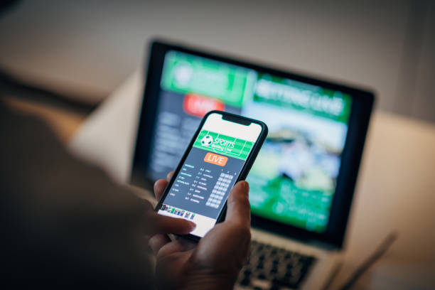 Mature man using mobile app for live betting and online gambling and watching a sports match